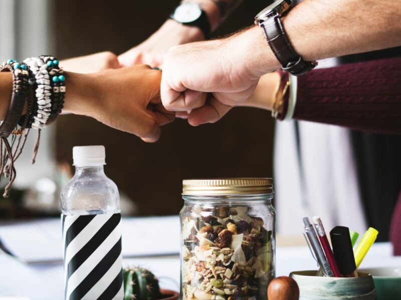 teamwork-hands-fist-tap-over-a-desk-with-nuts-1000x1000.jpg